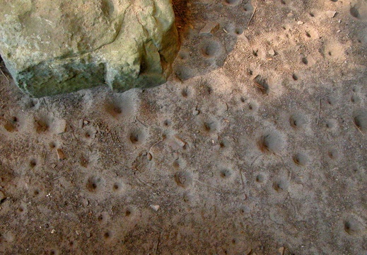 Sand floor beneath rock house lip has pitted impressions from repeated, steady water dripping.